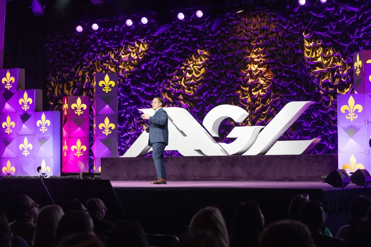 Speaker on the AAGL Global Congress stage with purple-and-gold event branding and large AAGL letters